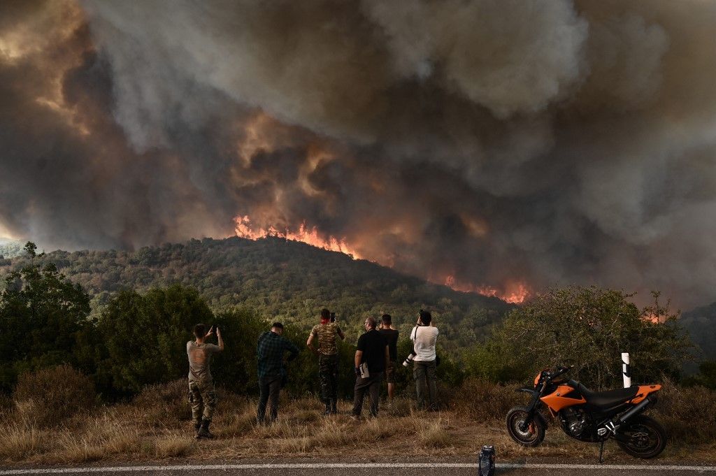 People look at the wildfire raging in a forest in Sikorahi, near Alexandroupoli, northern Greece, on August 23, 2023. Greek firefighters on August 23, 2023 struggled to contain uncontrolled fires throughout the country for a fifth day, several of them bordering an acrid, smoke-filled Athens. (Photo by Sakis MITROLIDIS / AFP)