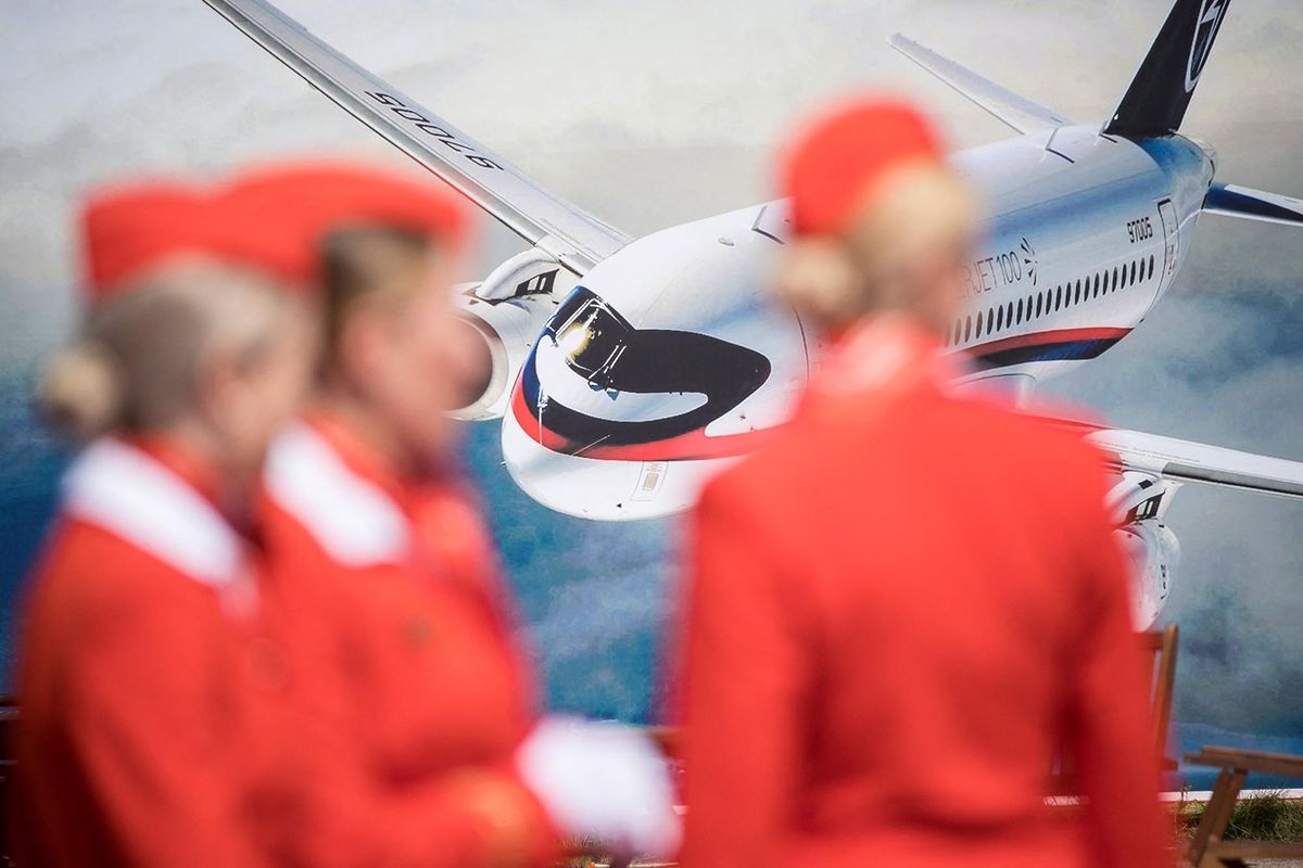 Russian airlines Aeroflot air hostesses stand in front of an advertizing board depicting the new Russian Sukhoi Superjet 100 airliner on July 18, 2017 on the opening day of the annual air show MAKS 2017 in Zhukovsky, some 40 km outside Moscow. (Photo by Mladen ANTONOV / AFP)