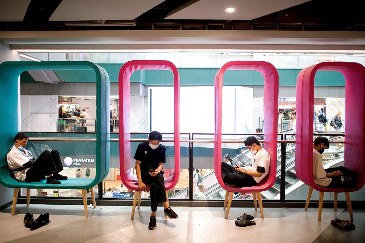 A man (2nd-L) checks his smartphone as others rest on chairs inside a shopping mall in Bangkok on April 27,2023. (Photo by MANAN VATSYAYANA / AFP)