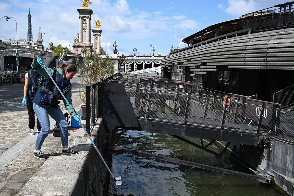 An employee of the company Fluidion collects a sample of water from the Seine to analyse its composition ahead of the 2024 Paris Olympics, near the Pont Alexandre III in Paris, on August 4, 2023. A swimming training event supposed to occur as a test ahead of the 2024 Paris Olympics on August 4, was canceled due to the poor quality of the Seine river's water. (Photo by Bertrand GUAY / AFP)