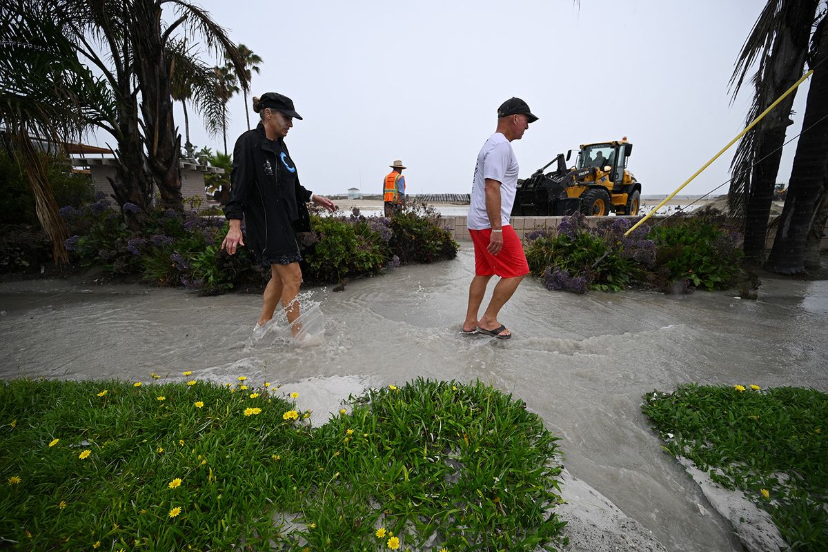 Residents walk through flood water near the beach in Long Beach, California, on August 20, 2023. Hurricane Hilary weakened to a tropical storm on August 20, 2023, as it barreled up Mexico's Pacific coast, but was still likely to bring life-threatening flooding to the typically arid southwestern United States, forecasters said. Authorities reported at least one fatality in northwestern Mexico, where Hilary lashed the Baja California Peninsula with heavy rain and strong winds. (Photo by Robyn Beck / AFP)