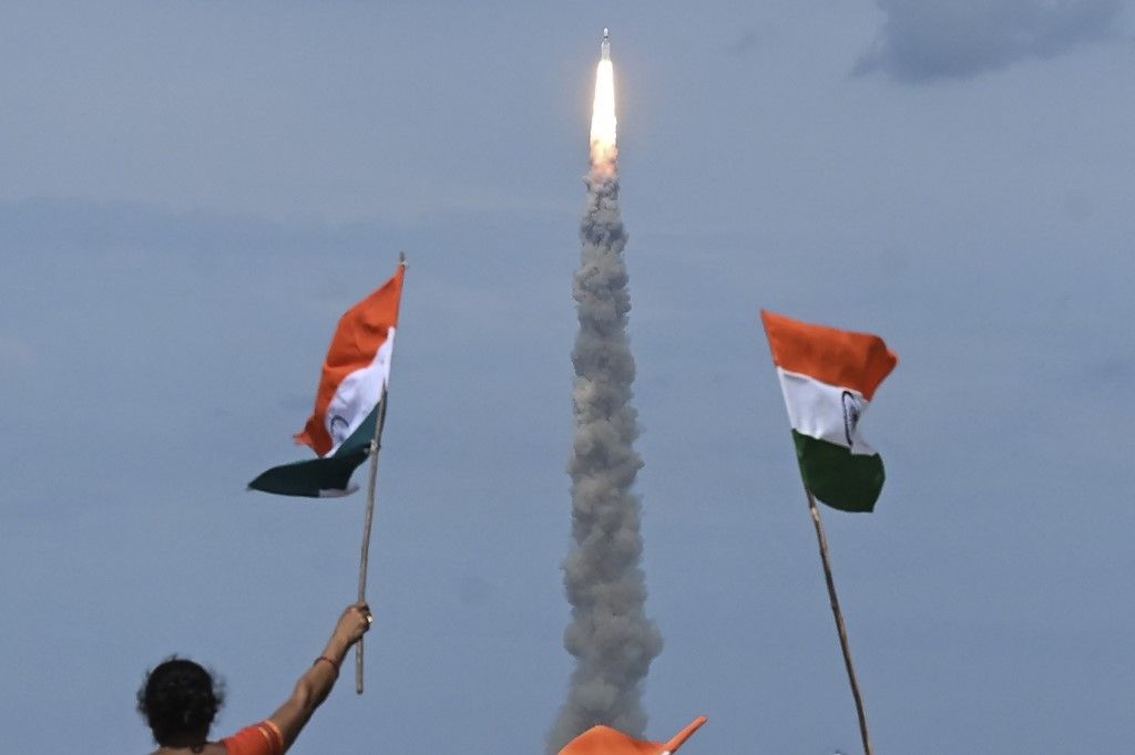 People wave Indian flags as an Indian Space Research Organisation (ISRO) rocket carrying the Chandrayaan-3 spacecraft lifts off from the Satish Dhawan Space Centre in Sriharikota, an island off the coast of southern Andhra Pradesh state on July 14, 2023. India launched a rocket on July 14 carrying an unmanned spacecraft to land on the Moon, its second attempt to do so as its cut-price space programme seeks to reach new heights. (Photo by R.Satish BABU / AFP)