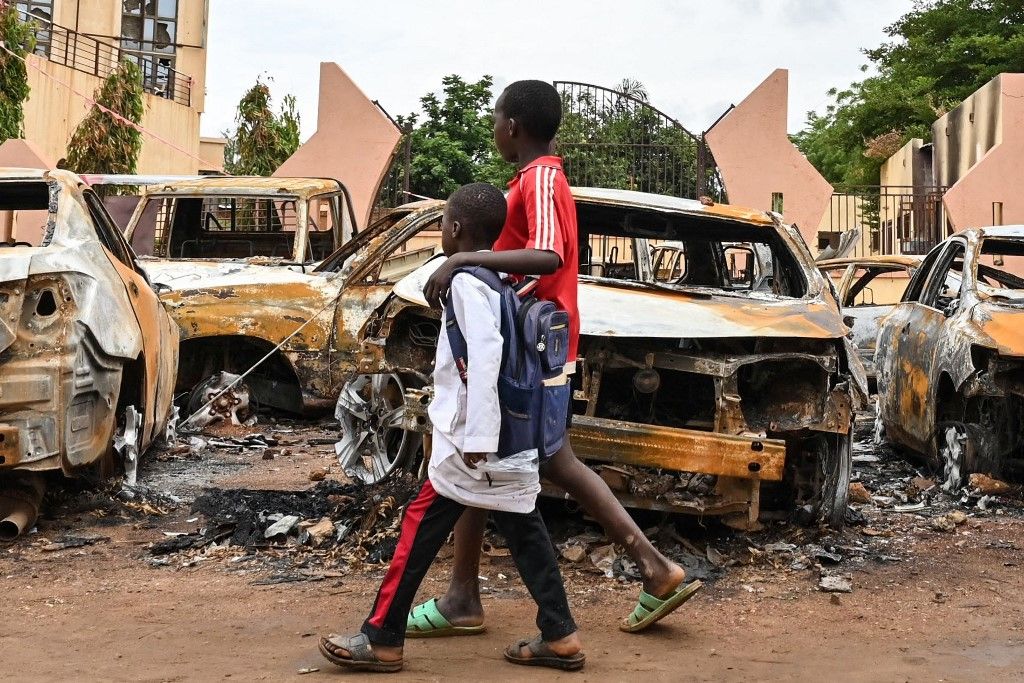 Children walk past burned cars outside the headquarters of president Bazoum's Nigerien Party for Democracy and Socialism in Niamey on August 7, 2023. Niger's military rulers were on Monday in defiance of an ultimatum to restore the elected government as the threat of possible military intervention was still on the table. (Photo by AFP)