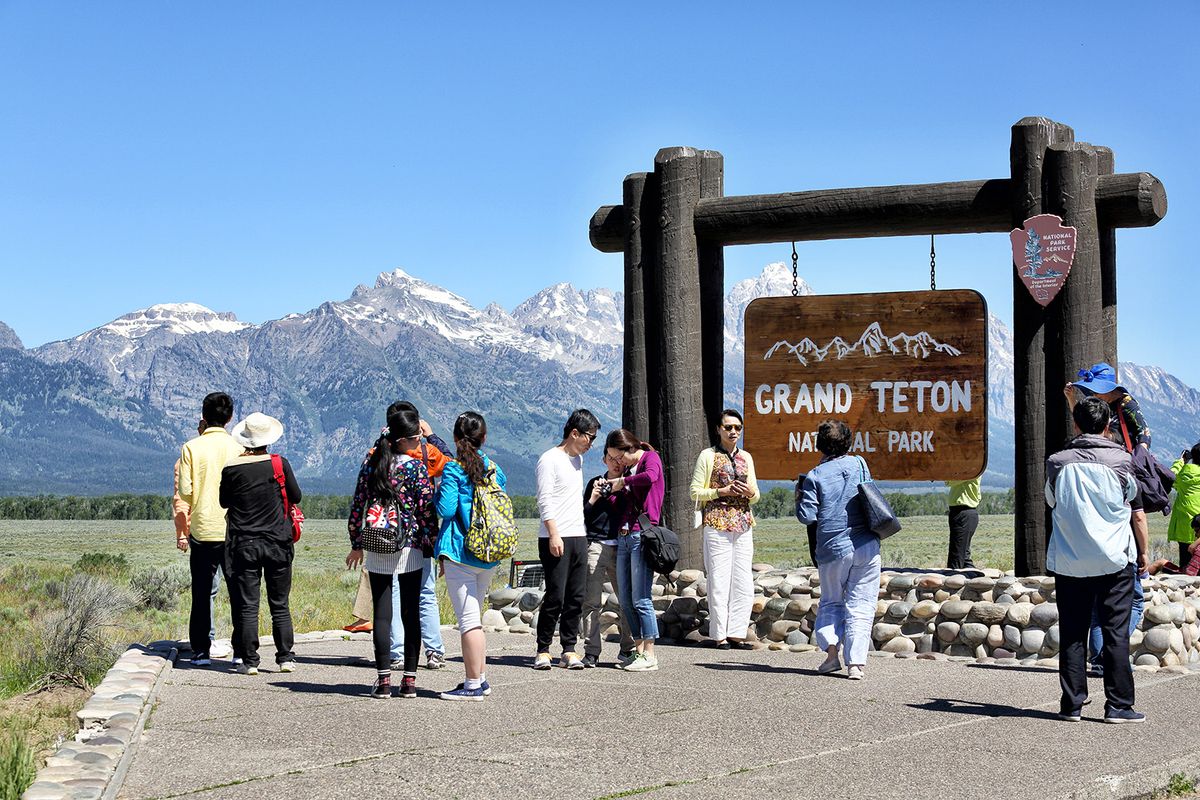 Jackson, Wyoming, USA  June 26, 2016 A group of adult asian tourists pose for pictures at the entrance sign for Grand Teton National Park near Jackson Wyoming. 