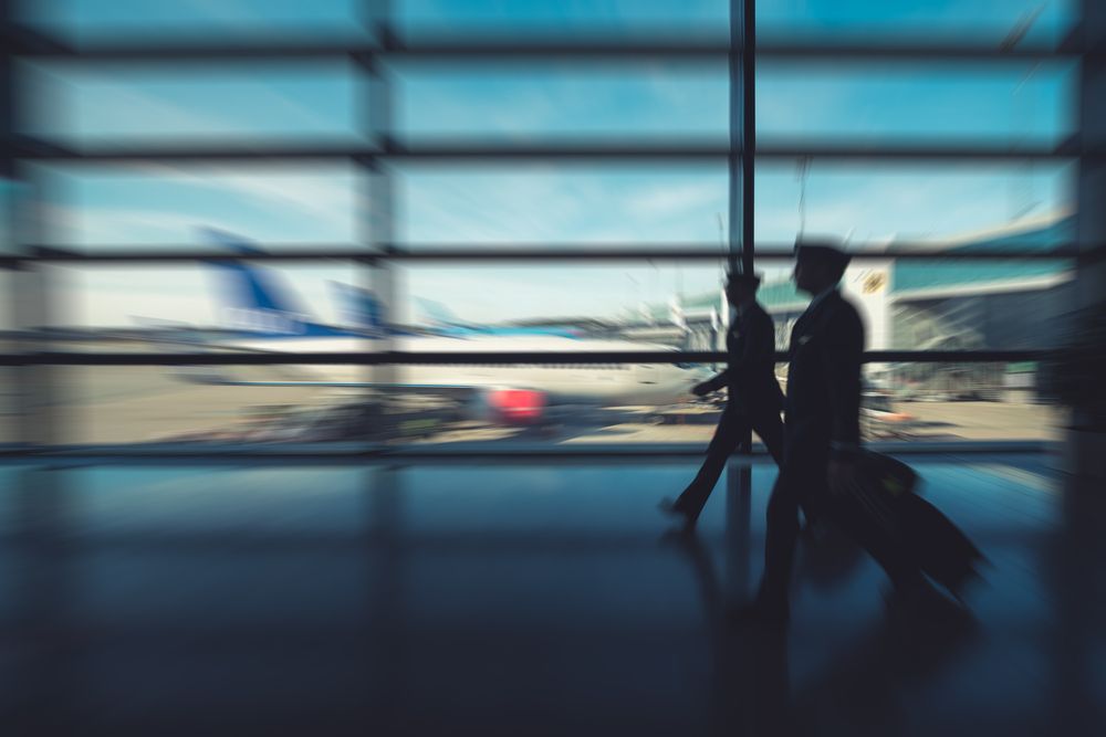 Silhouette,Of,Two,Pilots,Walking,In,Airport,Terminal,With,Airplanes