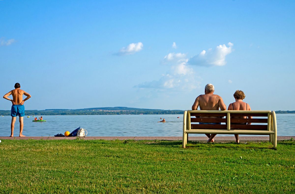 Old couple sitting on a bench looking at the lake Balaton on the beach in Hungary with copy space 