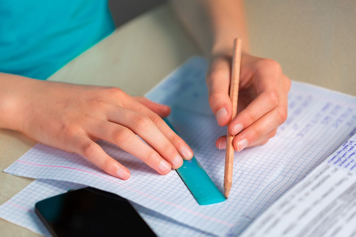 Teenage girl left-handed drawing with a ruler, close up on hands. Studying, education and exam concept