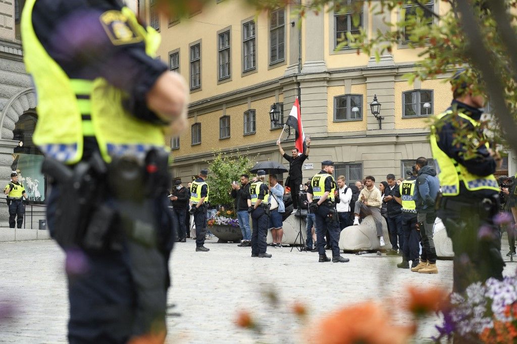 Policemen stand next to demonstrators, among them a protester (background, C) holding the flag of Iraq, at Mynttorget square in Stockholm, Sweden, on July 31, 2023. Two men set the Koran alight outside parliament in Stockholm, an AFP reporter saw, at a protest similar to previous ones that have sparked tensions between Sweden and Middle Eastern countries. (Photo by Oscar OLSSON / TT News Agency / AFP) / Sweden OUT