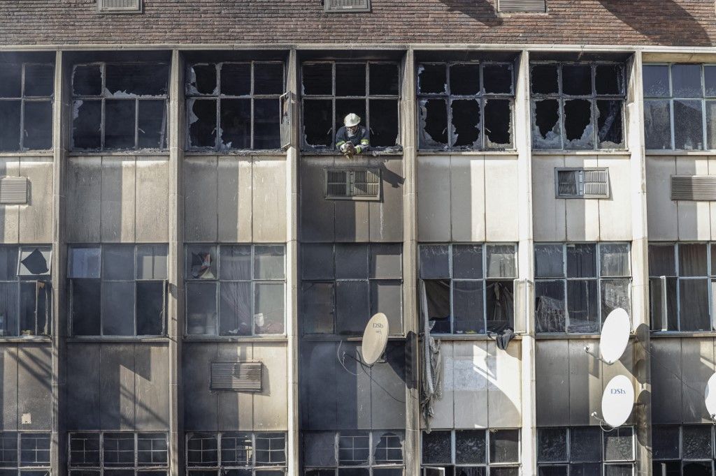 A firefighter looks out of broken windows at the scene of a fire in a building in Johannesburg on August 31, 2023. At least 20 people have died and more than 40 were injured in a fire that engulfed a five-storey building in central Johannesburg on August 31, 2023, the South African city's emergency services said. (Photo by Michele Spatari / AFP)