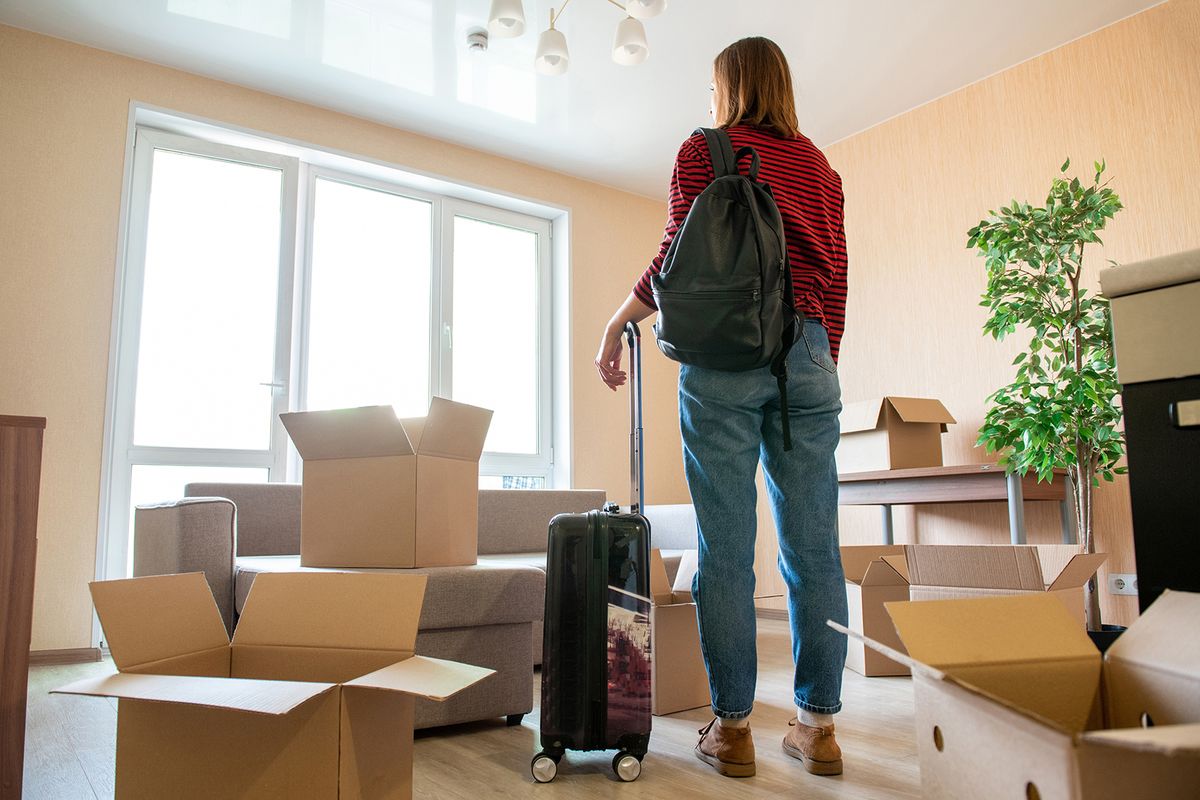 A,Woman,With,A,Suitcase,In,Her,Hands,Stands,InA woman with a suitcase in her hands stands in her new apartment. The concept of moving to a new place of residence or moving out of an old home