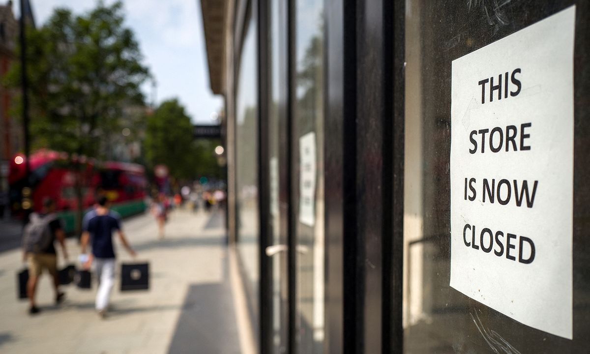 Pedestrians carry shopping bags as they walk past a sign in the window of a store alerting customers that the shop has closed-down, in London on August 12, 2020. Britain's economy contracted by a record 20.4 percent in the second quarter with the country in lockdown over the novel coronavirus pandemic, official data showed Wednesday.  "It is clear that the UK is in the largest recession on record," the Office for National Statistics said. Britain officially entered recession in the second quarter after gross domestic product (GDP) contracted by 2.2 percent in the first three months of the year. (Photo by Tolga AKMEN / AFP)