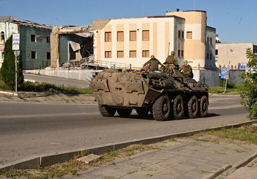 TOPSHOT - Ukrainian servicemen ride atop of an armored personel carrier (APC) past a destoyed building in the town of Kupiansk, Kharkiv region on August 17, 2023, amid the Russian invasion of Ukraine. The head of the region Oleg Synegubov said that Russian forces had shelled Zaoskillya, a suburb just east of Kupiansk, killing a woman born in 1962. "Another woman, born in 1963, suffered shrapnel wounds. Medics provided assistance to the injured on the spot," he wrote on social media. (Photo by SERGEY BOBOK / AFP)