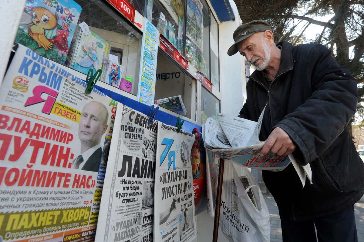 An elderly man looks through a newspaper at a kiosk with Russian newspapers displayed outside in the Crimean port of Sevastopol on March 27, 2014.  The Crimean crisis has sparked the most explosive East-West confrontation since the Cold War and fanned fears in Kiev that Russian President Vladimir Putin now intends to push his troops into southeast Ukraine. AFP PHOTO/ VIKTOR DRACHEV (Photo by VIKTOR DRACHEV / AFP)