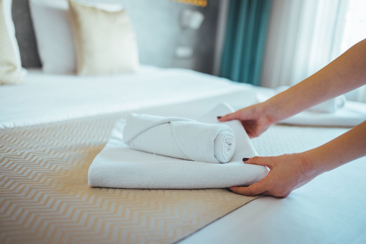 Female,Hand,Set,Up,White,Bed,Sheet,In,Bedroom.,Close-upFemale Hand set up white bed sheet in bedroom. Close-up of a maid's hands making bed in a hotel room. Making Bed. Maid working making the bed at a hotel. 