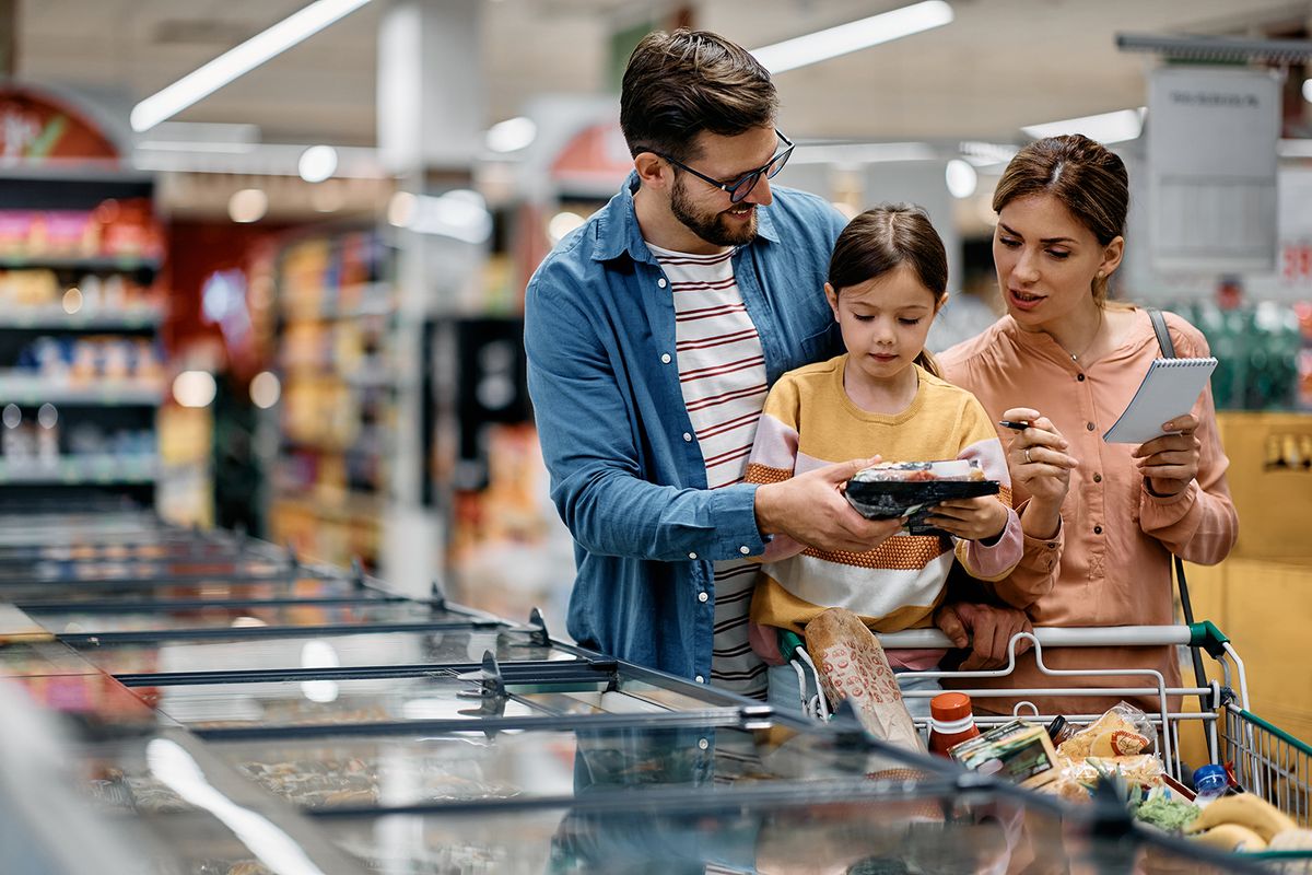 Little,Girl,And,Her,Parents,Choosing,Groceries,While,Shopping,AtLittle girl and her parents choosing groceries while shopping at supermarket. Copy space.