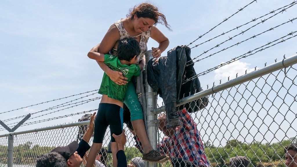 (FILES) A mother helps her child over the barbed wire fence in Eagle Pass, Texas, after crossing into the US from Mexico on August 25, 2023. (Photo by SUZANNE CORDEIRO / AFP)