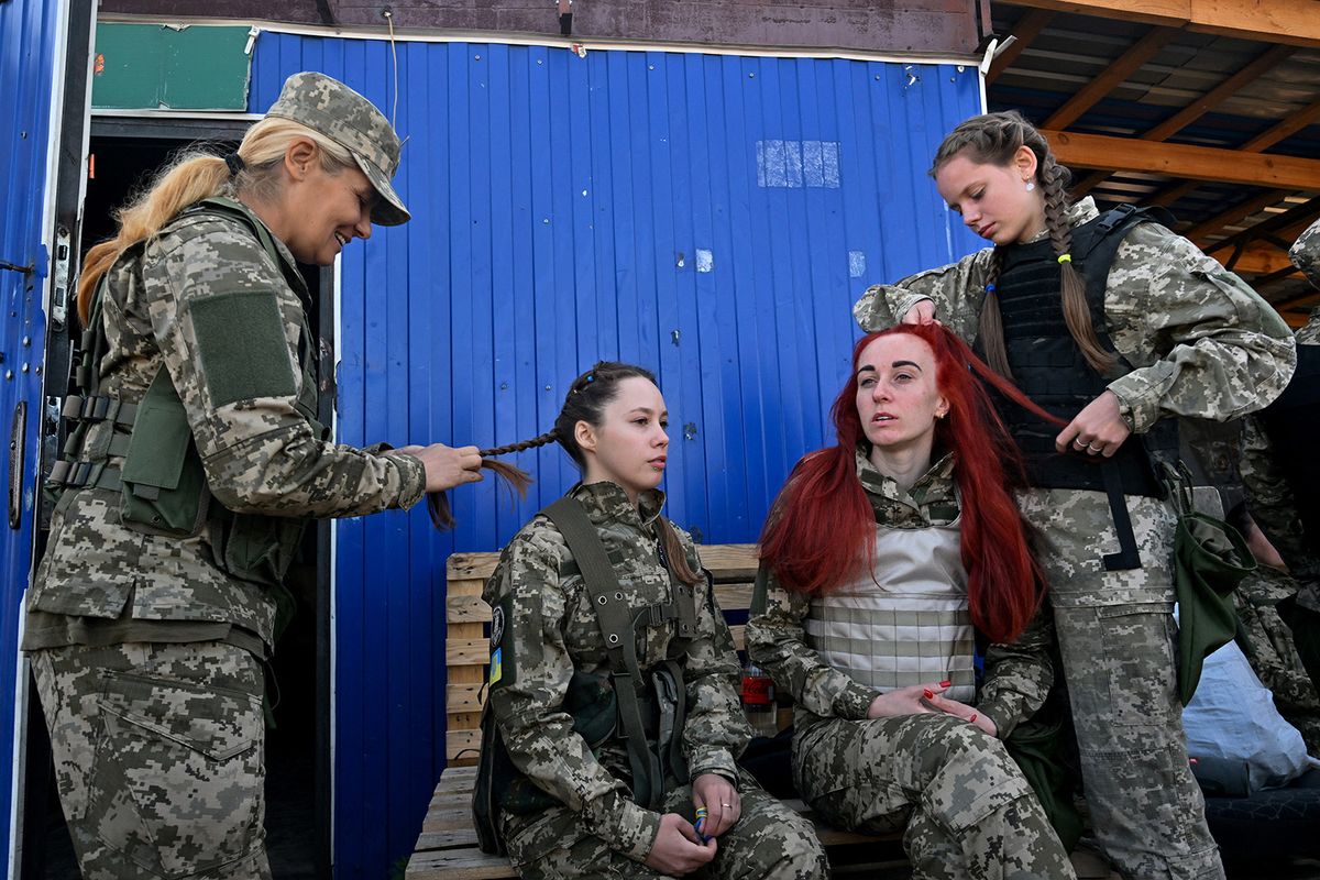 Female Ukrainian cadets, wearing new military uniforms designed specially for women, have their hair braided as they take part in a training during the "Uniform matters" event organised to present the outfit and test it under military training conditions, on the outskirts of Kyiv on July 12, 2023. (Photo by Sergei SUPINSKY / AFP)