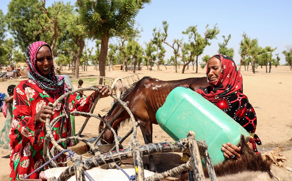 Two nomadic women load 20-litre cans of water onto the back of a donkey and carry them to their homes one kilometre from the water well in the Toukra camp in N'Djamena, Chad, on June 10, 2022. In Chad, many nomadic herders are settling down, discouraged by global warming, lack of access to pasture and community conflicts. (Photo by AURELIE BAZZARA-KIBANGULA / AFP)