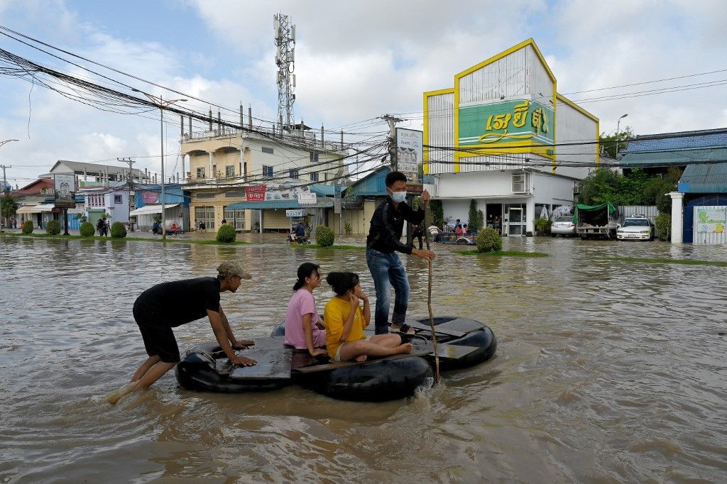 People sit on a raft as they make their way through floodwaters on the outskirts of Phnom Penh on October 28, 2021, following heavy monsoon rains. (Photo by TANG CHHIN Sothy / AFP)