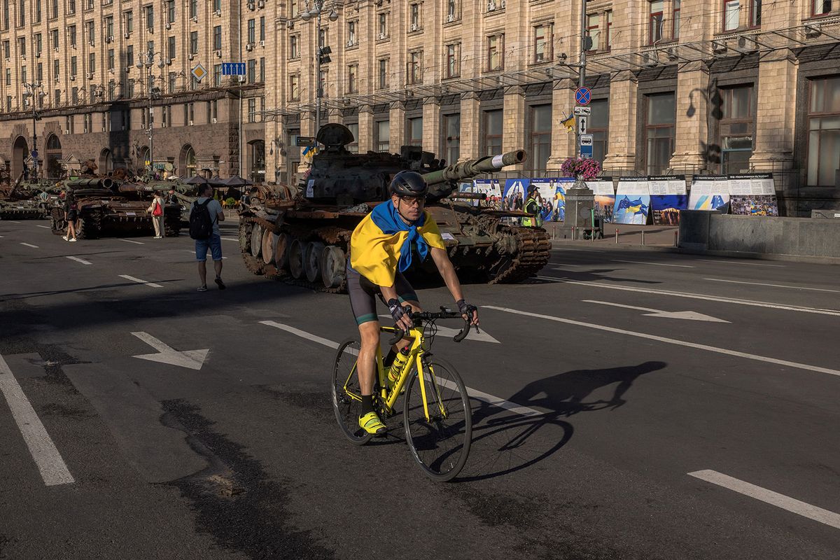 A man wearing Ukraine’s national flag rides a bicycle past destroyed Russian armoured military vehicles on display in Khreshchatyk street on Ukraine’s Independence Day in Kyiv, on August 24, 2023, amid the Russian invasion of Ukraine. (Photo by Roman Pilipey / AFP)