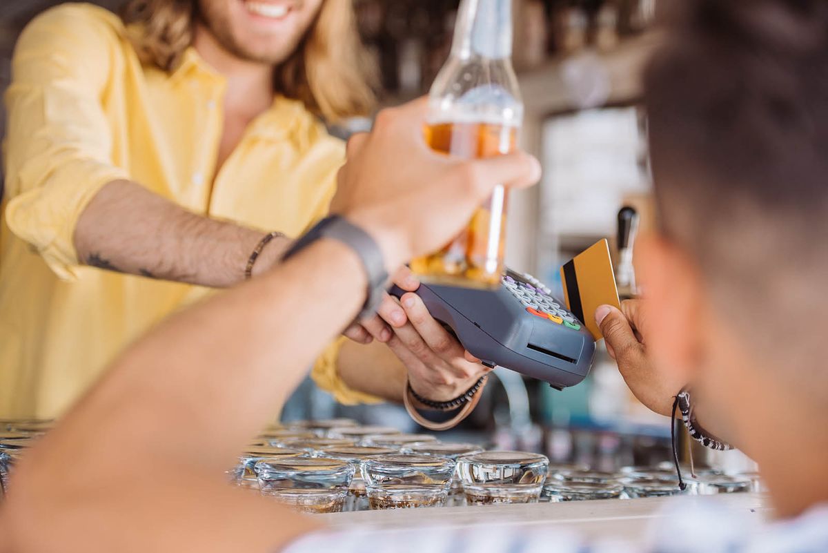 Cropped,Shot,Of,Young,Man,Holding,Beer,Bottle,And,Payingcropped shot of young man holding beer bottle and paying with credit card at beach bar