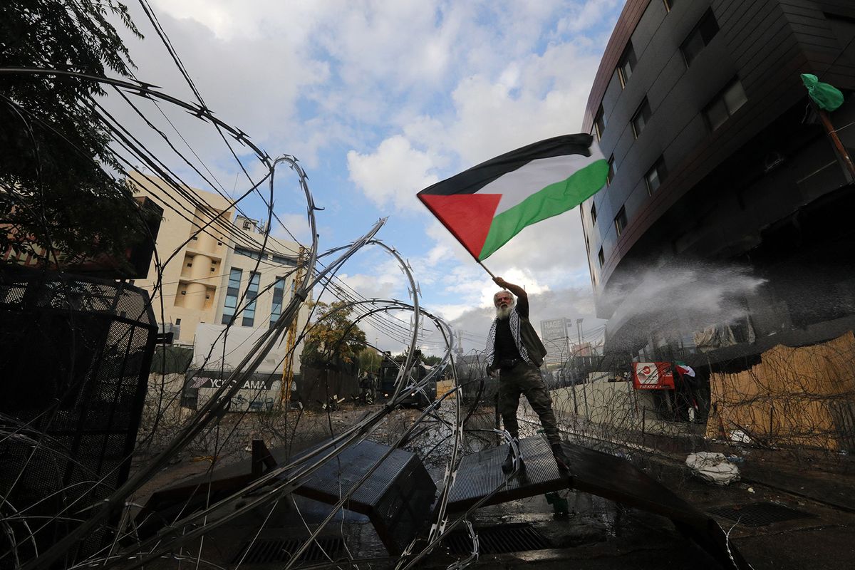 A man waves a Palestinian flags as Lebanese security forces clash with protesters outside the US Embassy in Awkar east of Beirut, during a demonstration in solidarity with the Palestinians of the Gaza Strip, on October 18, 2023. Thousands rallied across the Arab and Muslim world on October 18 to protest the deaths of hundreds of people in a strike on a Gaza hospital that they blame on Israel, despite its denials. (Photo by Ibrahim AMRO / AFP)