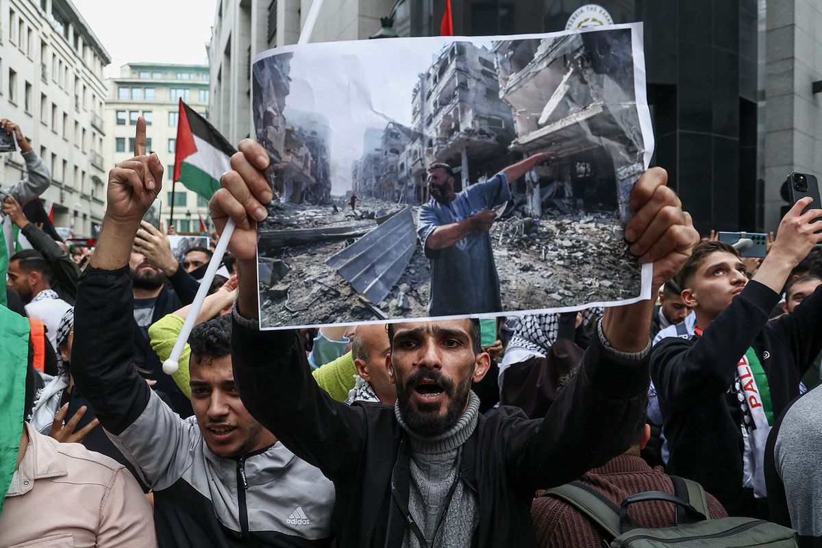 A protester holds a photograph taken by AFP photographer Mahmud Hams (of people inspecting the damage following an overnight Israeli airstrikes in the Gaza Strip) above his head during a demonstration against Israel's military operations in Gaza and in support of Palestinians, in Brussels on October 11, 2023. (Photo by Kenzo TRIBOUILLARD / AFP)