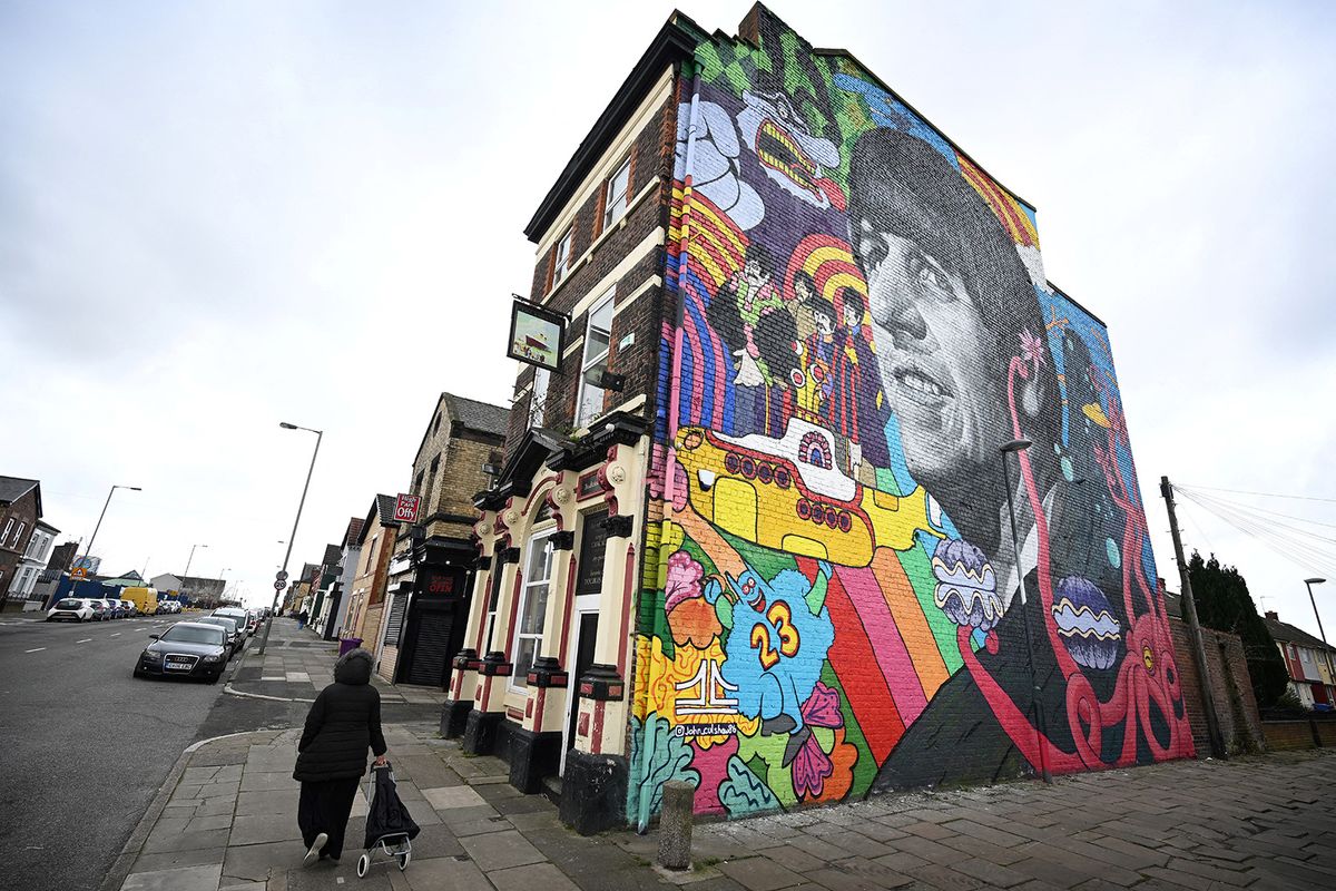 A pedestrian walks past a mural depicting former Beatles member Ringo Starr and painted by Liverpool artist John Culshaw, on the facade wall of The Empress Pub in Toxteth, Liverpool, north west England, on March 9, 2022. The mural has been painted close to places connected with the former Beatles including his birthplace and childhood home. (Photo by Paul ELLIS / AFP) / RESTRICTED TO EDITORIAL USE - MANDATORY MENTION OF THE ARTIST UPON PUBLICATION - TO ILLUSTRATE THE EVENT AS SPECIFIED IN THE CAPTION