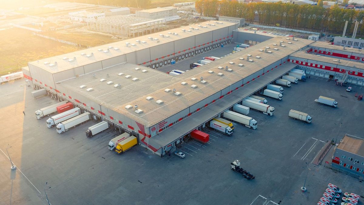 Aerial,View,Of,A,Logistics,Park,With,Warehouse,,Loading,HubAerial view of a logistics park with warehouse, loading hub and many semi trucks with cargo trailers standing at the ramps for load/unload goods at sunset. ipari park, logisztikai, park