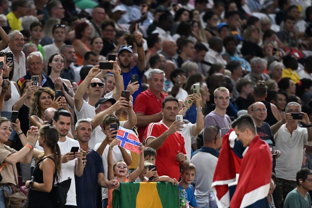 Fans use their phones to film as Norway's Jakob Ingebrigtsen celebrates with his national flag after winning the men's 5000m final during the World Athletics Championships at the National Athletics Centre in Budapest on August 27, 2023. (Photo by Jewel SAMAD / AFP)
