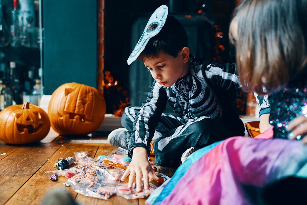 Two children sitting on a wooden floor looking at their sweets with pumpkins in the background. (Photo by Wholly Owned ISUK / Cultura Creative / Cultura Creative via AFP)