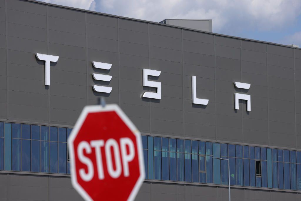 Tesla To Quadruple Production At Gruenheide PlantGRUENHEIDE, GERMANY - JULY 17: A stop sign stands near the Tesla logo at the Tesla factory on July 17, 2023 near Gruenheide, Germany. Tesla will reportedly present its plans tomorrow to expand production at the factory, from thee current level of approximately 250,000 cars per year to one million. The plan calls for the construction of a new assembly hall that will be the size of 60 soccer fields, which is likely to draw opposition from local communities.  (Photo by Sean Gallup/Getty Images)