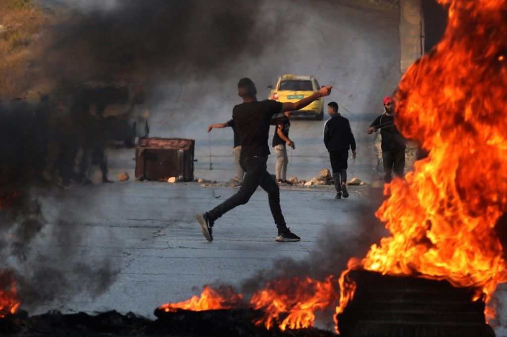 A Palestinian demonstrator throws rocks towards Israeli soldiers during clashes in the city of Ramallah in the occupied West Bank on October 8, 2023. Israel, reeling from the deadliest attack on its territory in half a century, formally declared war on Hamas on October 8, as the conflict's death toll surged to 1,000 after the Palestinian militant group launched a massive surprise assault from Gaza. (Photo by Jaafar ASHTIYEH / AFP)