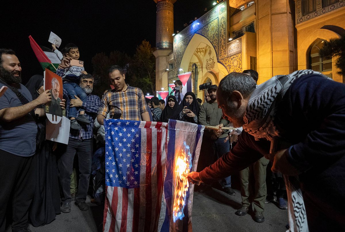 An Iranian protester burn the U.S. flag and an Israeli flag in a rally protesting the Israeli attacks on Gaza city, at the Palestine square in downtown Tehran, October 20, 2023.  (Photo by Morteza Nikoubazl/NurPhoto) (Photo by Morteza Nikoubazl / NurPhoto / NurPhoto via AFP)