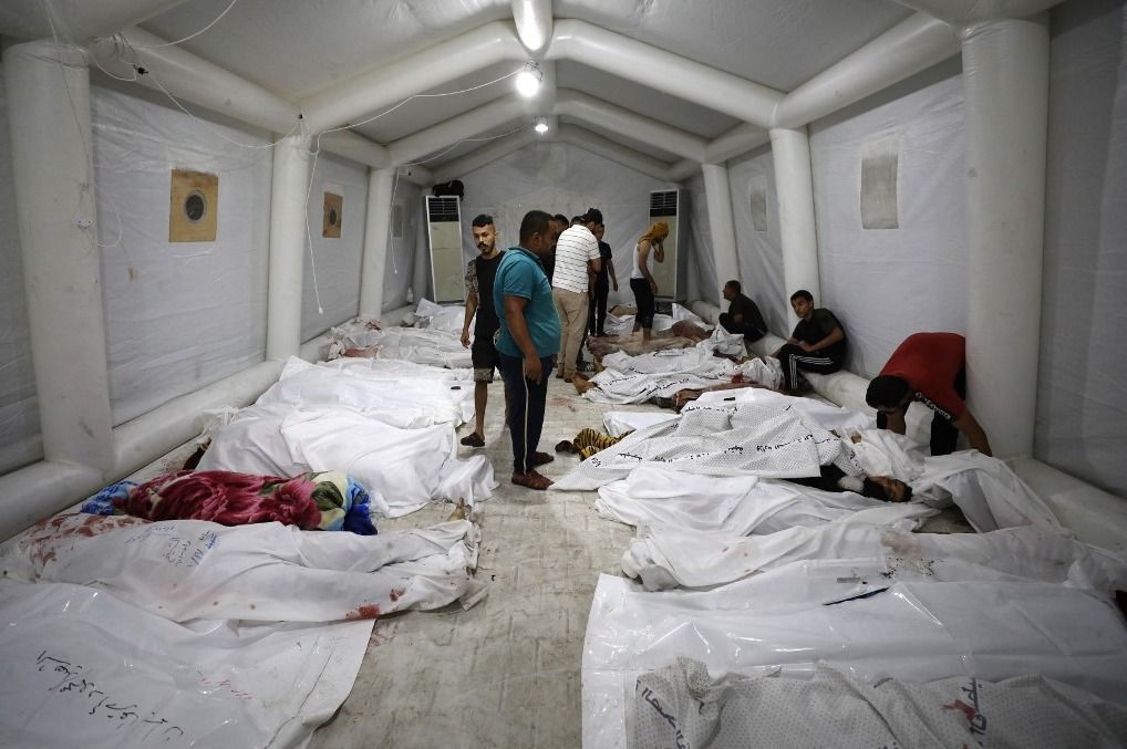 EDITORS NOTE: Graphic content / People stand over bodies of Palestinians killed in a strike on the Ahli Arab hospital in central Gaza after they were transported to Al-Shifa hospital, on October 17, 2023. Israel and Palestinians traded blame for the incident, which an "outraged and deeply saddened" US President Joe Biden denounced while en route to the Middle East. (Photo by Dawood NEMER / AFP)