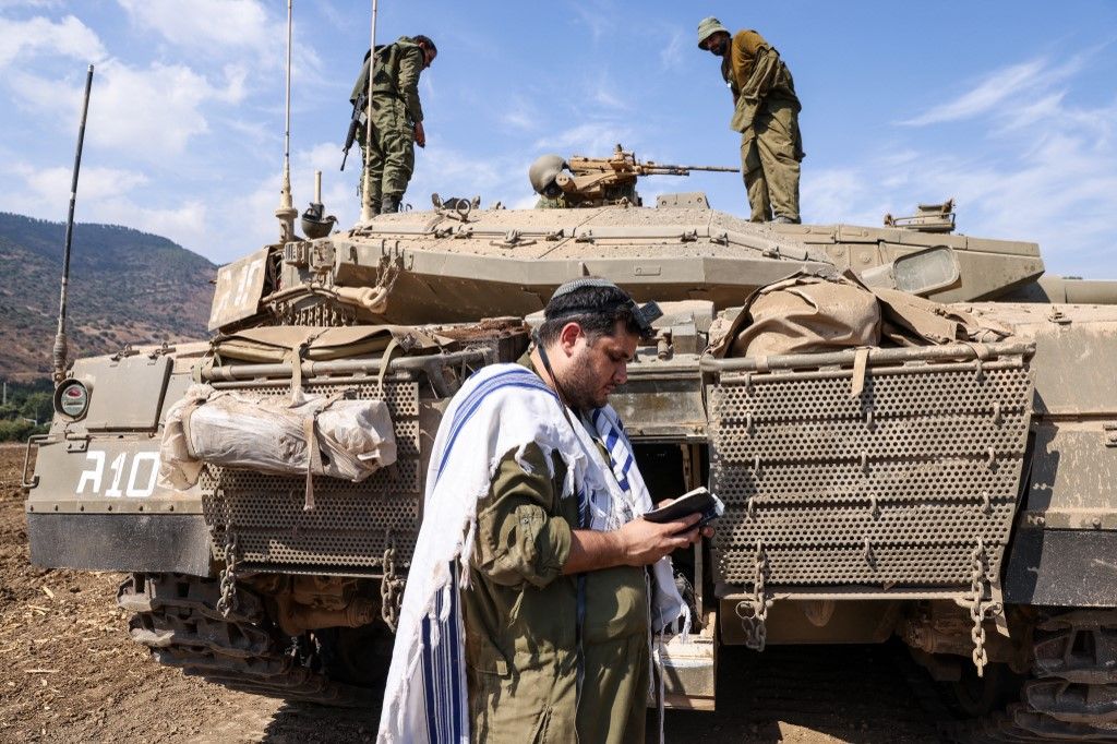 EDITORS NOTE: Graphic content / An Israeli sodleir prays standing in front of a Merkava tank on the outskirts of the northern town of Kiryat Shmona near the border with Lebanon on October 8, 2023. Lebanon's Hezbollah and Israel said they traded cross-border fire on October 8, as Israel fought the Shiite movement's ally Hamas on its southern flank a day after militants from the Palestinian group stormed its Gaza frontier. (Photo by JALAA MAREY / AFP)