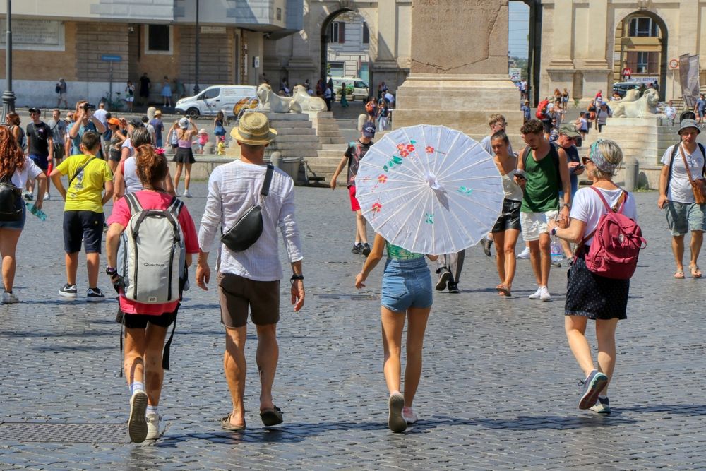 Tourist,Protect,Themselves,From,The,Sun,With,Umbrellas,And,Hats