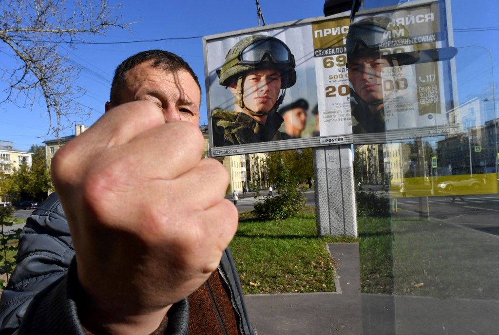 A man gestures in front of a billboard promoting contract army service reading 'Join yours' in Saint Petersburg on October 10, 2023. (Photo by Olga MALTSEVA / AFP)