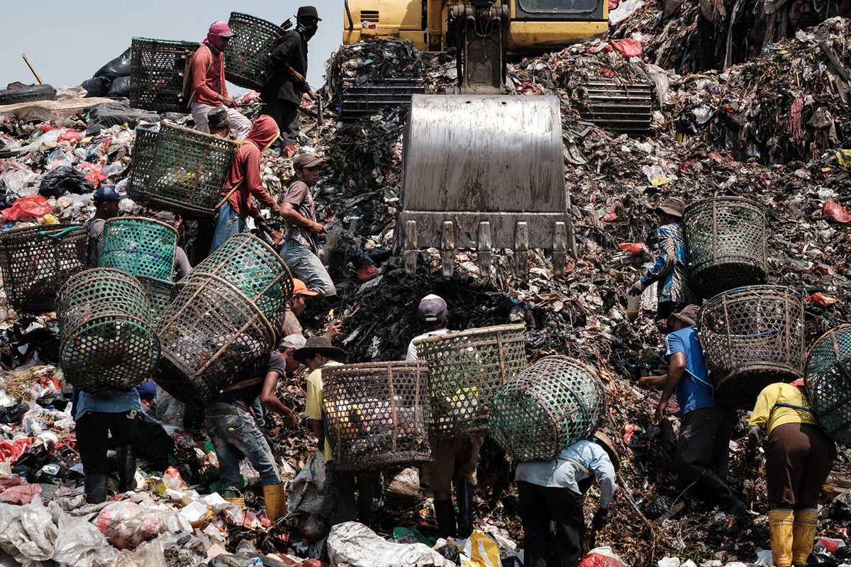 This picture taken on September 14, 2023 shows registered scavengers, who mainly collect plastic waste to sell, waiting as a crane moves waste up to a higher level at the Bantar Gebang landfill, which is the size of 200 football pitches and receives 7,500 tonnes of waste from Jakarta every day, in Bekasi, on the outskirts of Jakarta. Home to around 30 million people, the sprawling megalopolis of Jakarta is facing a trash crisis with its main Bantar Gebang dump site, one of the world's biggest, close to capacity. (Photo by Yasuyoshi CHIBA / AFP) / TO GO WITH Indonesia-environment-waste, PHOTO ESSAY