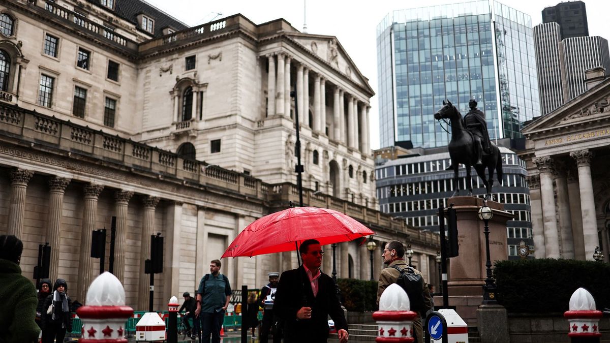 A pedestrian with an umbrella walks by the Bank of England building (rear), in the financial district, central London, on November 2, 2023. (Photo by HENRY NICHOLLS / AFP)BRITAIN-INFLATION-RATE-BANKING-BOE