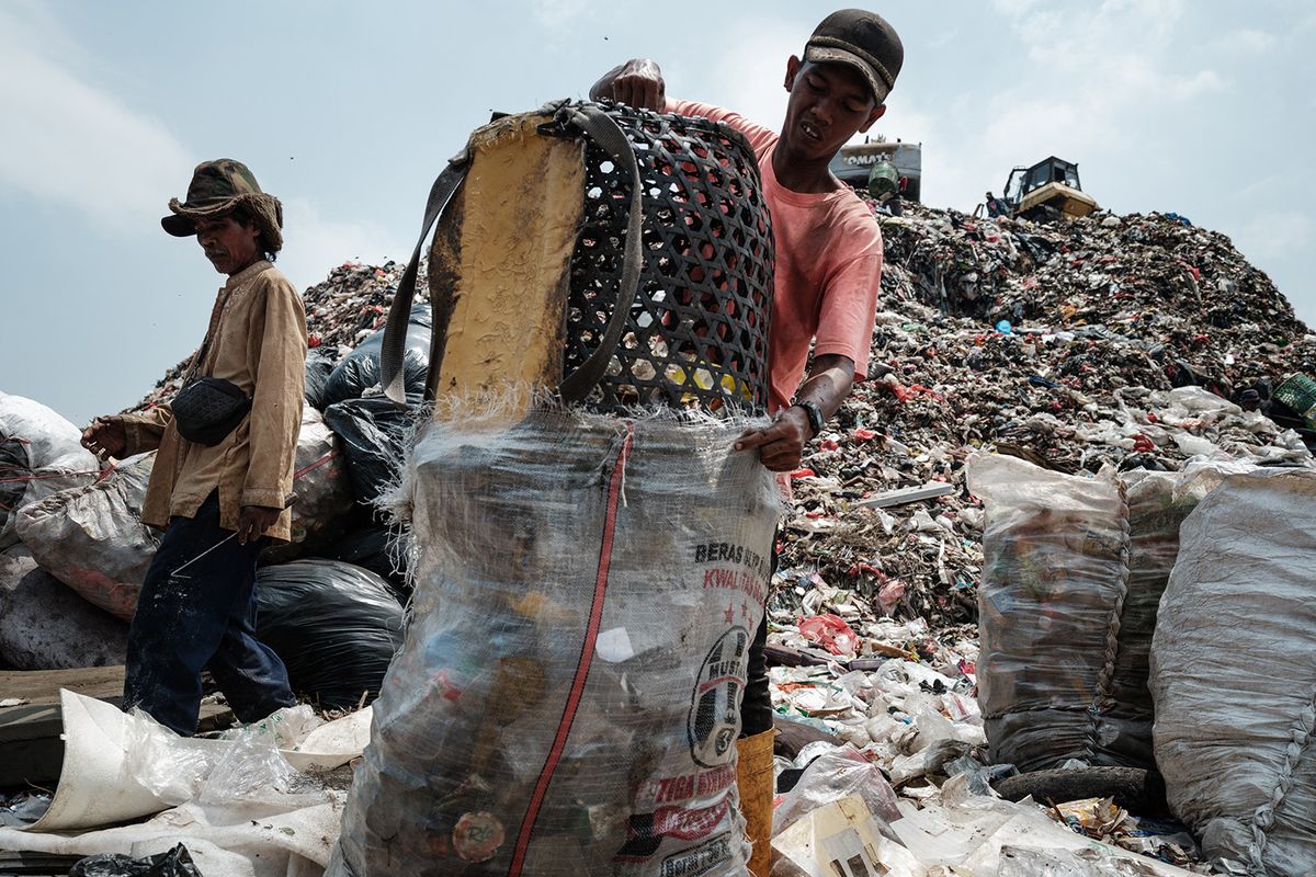 This picture taken on September 14, 2023 shows a registered scavenger, who mainly collects plastic waste to sell, transferring waste from his basket into a sack at the Bantar Gebang landfill, which is the size of 200 football pitches and receives 7,500 tonnes of waste from Jakarta every day, in Bekasi, on the outskirts of Jakarta. Home to around 30 million people, the sprawling megalopolis of Jakarta is facing a trash crisis with its main Bantar Gebang dump site, one of the world's biggest, close to capacity. (Photo by Yasuyoshi CHIBA / AFP) / TO GO WITH Indonesia-environment-waste, PHOTO ESSAY
