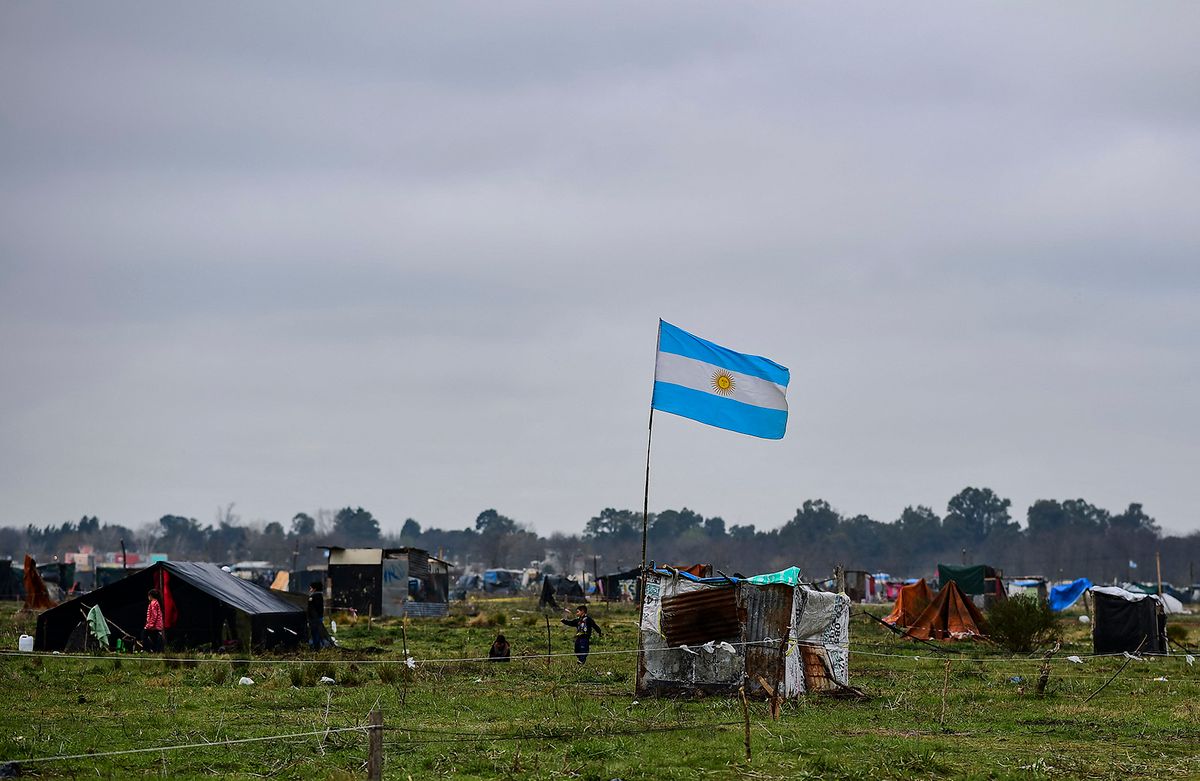 An Argentine flag flutters in the wind above a tiny house made of corrugated iron sheets in land occupied by homeless people outside Guernica, in the province of Buenos Aires, south of the Argentine capital, on August 28, 2020 amid rising poverty in an economic crisis exacerbated by the COVID-19 novel coronavirus pandemic. Outdoors or under makeshift tents, about 2,500 people have been defying justice, and COVID-19, for more than a month, when they occupied empty lots in Buenos Aires Province, the most populous of the country and where the pandemic is hitting the hardest. Scattered in over 100 hectares of vacant land, children run around and adults talk, while the police guards the area. Prevention measures against the novel coronavirus barely exist here. (Photo by Ronaldo SCHEMIDT / AFP)