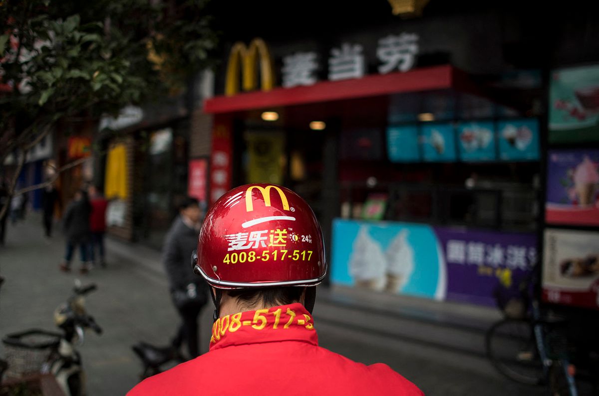 A delivery man stands in front of a McDonald's fast food restaurant in Shanghai on January 9, 2017. US fast-food giant McDonald’s will sell a controlling stake in its China and Hong Kong business for up to 2.08 billion USD to a consortium including state-owned Citic and the Carlyle Group, it was announced on January 9. (Photo by Johannes EISELE / AFP)