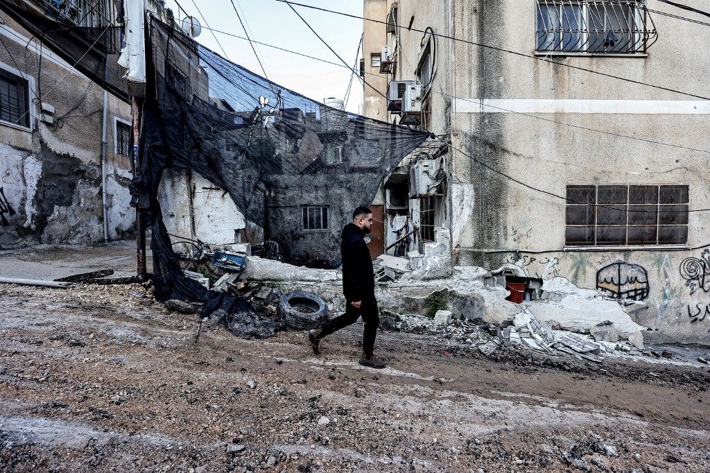 A Palestinian man walks past a damaged building in the aftermath of an Israeli raid in the Nur Shams camp for Palestinian refugees near the northern city of Tulkarm in the occupied West Bank on December 26, 2023. The Israeli operation in the Palestinian refugee camp in the north of the occupied West Bank left six people dead and several others wounded according to the Palestinian ministry of health. According to the official Palestinian news agency Wafa, the six people were killed by Israeli air strikes on the refugee camp where Israeli soldiers were also deployed. (Photo by Zain JAAFAR / AFP)