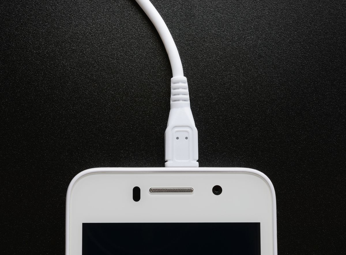 White,Smart,Phone,Charging,With,Cable,On,The,Black,Table