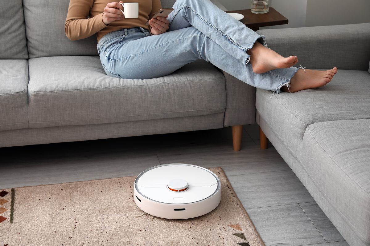Modern,Robot,Vacuum,Cleaner,Near,Sofa,With,Resting,Woman,In
