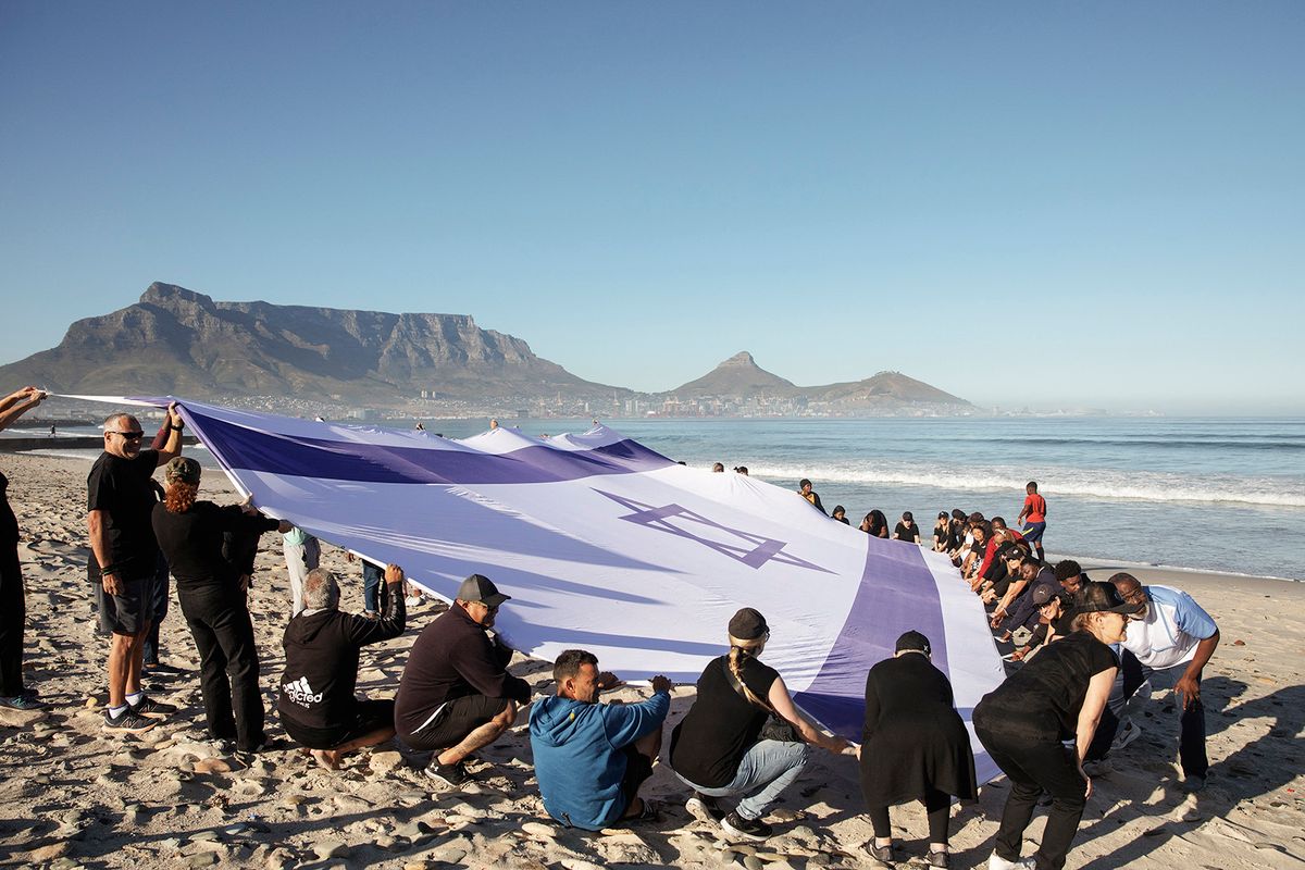 Jews and Christians from Cape Town hold a giant Israeli flag in support of Israel at Lagoon beach in Cape Town, on December 16, 2023. Thousands of civilians, both Palestinians and Israelis, have died since October 7, 2023, after Palestinian Hamas militants based in the Gaza Strip entered southern Israel in an unprecedented attack triggering a war declared by Israel on Hamas with retaliatory bombings on Gaza. (Photo by STRINGER / AFP)