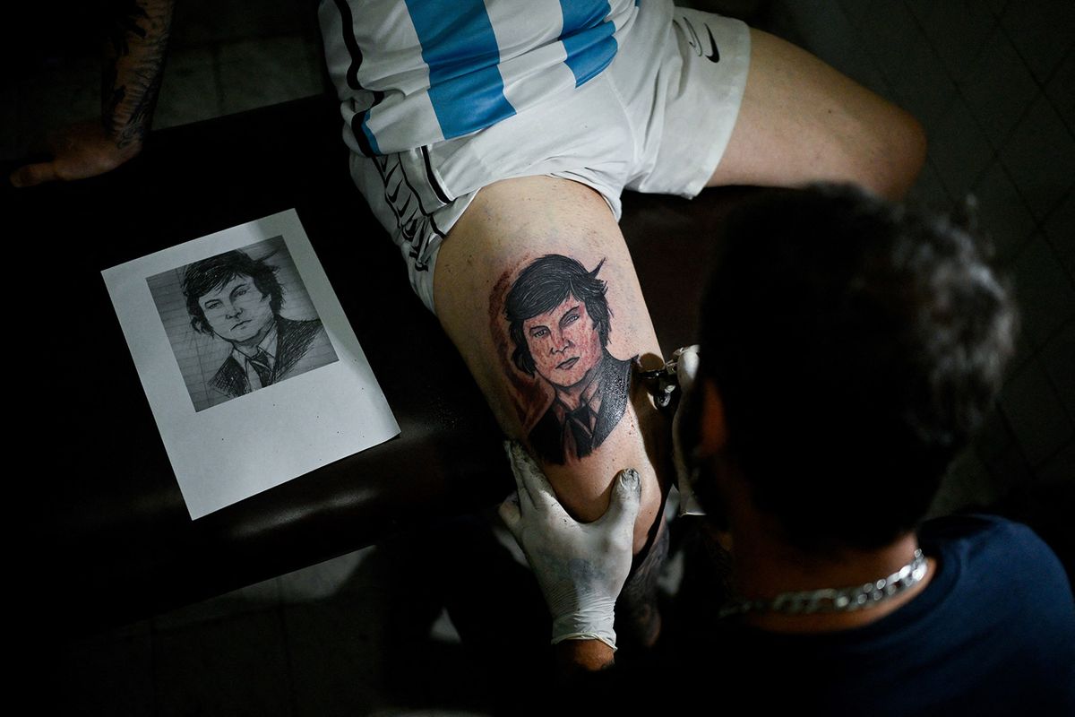 Service station employee Pablo Vega, 48, voter of president-elect Javier Milei, gets his leg tattooed with an image of Milei's face in La Matanza, Buenos Aires province, Argentina on December 7, 2023. Samir Santa Cruz, a 21-year-old delivery man, pedals day and night to bring some money home. "It was a relief that (Javier) Milei won; I trust him," he says, hopefully, like other young Argentines, the sector that most supports the president-elect. (Photo by LUIS ROBAYO / AFP)