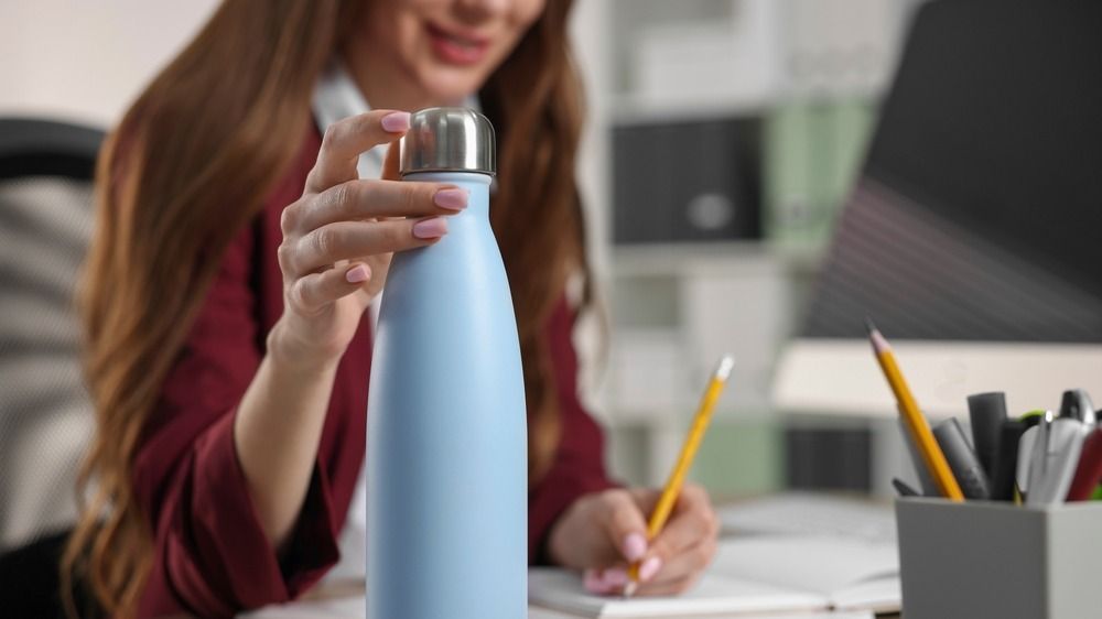 Woman,Holding,Thermos,Bottle,At,Workplace,,Closeup