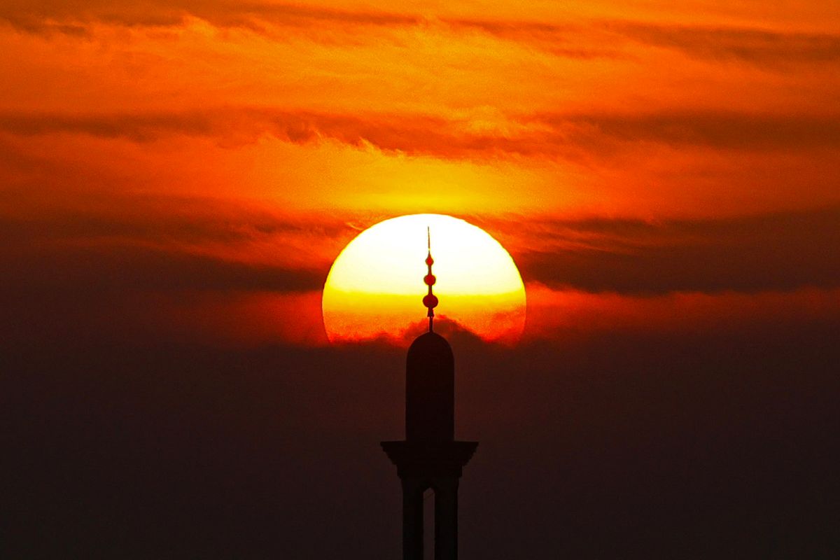 A picture taken from Rafah on the southern Gaza Strip on December 6, 2023, shows the minaret of a mosque silhouetted against the setting sun amid continuing battles between Israel and the Palestinian militant group Hamas. Israeli forces were encircling southern Gaza's main city on December 6, battling Hamas militants through streets and buildings in some of the most intense combat of the two-month war. (Photo by MAHMUD HAMS / AFP)